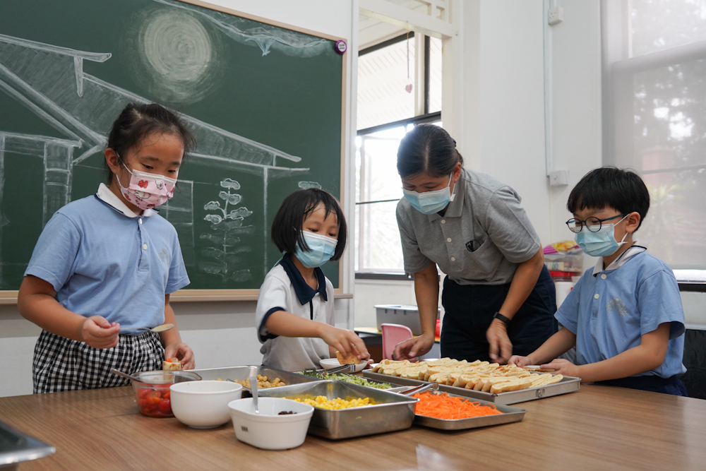 Students inserting the fillings of the Vegetarian Pita Sandwich under the watchful eye of Centre Manager Ms Lim Siew Lee. (Photo by Chan May Ching)       